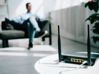 selective focus of black plugged router on white table and businessman sitting on sofa