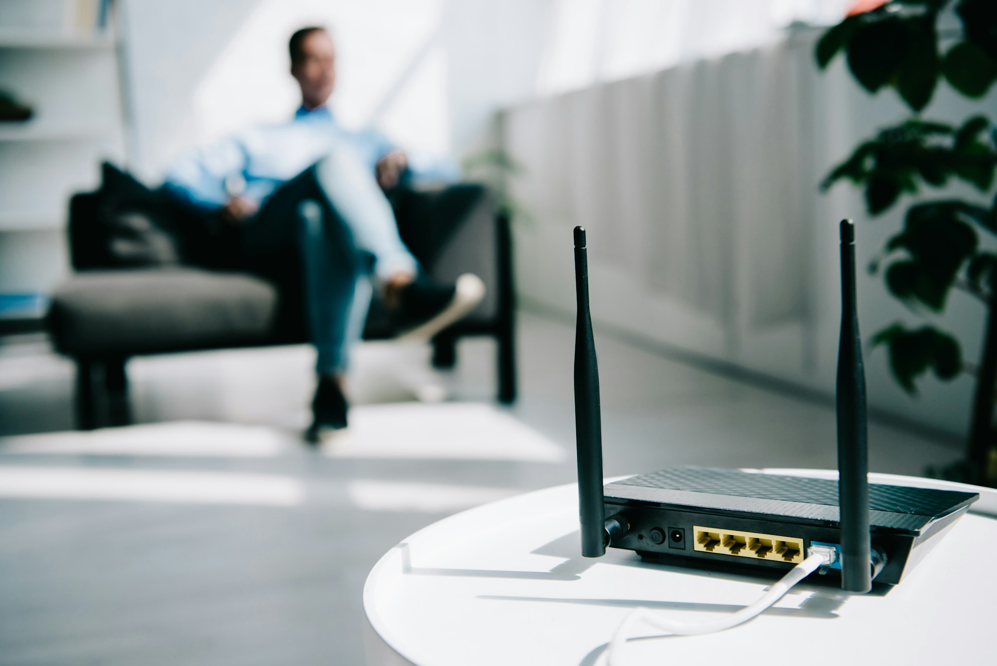 selective focus of black plugged router on white table and businessman sitting on sofa